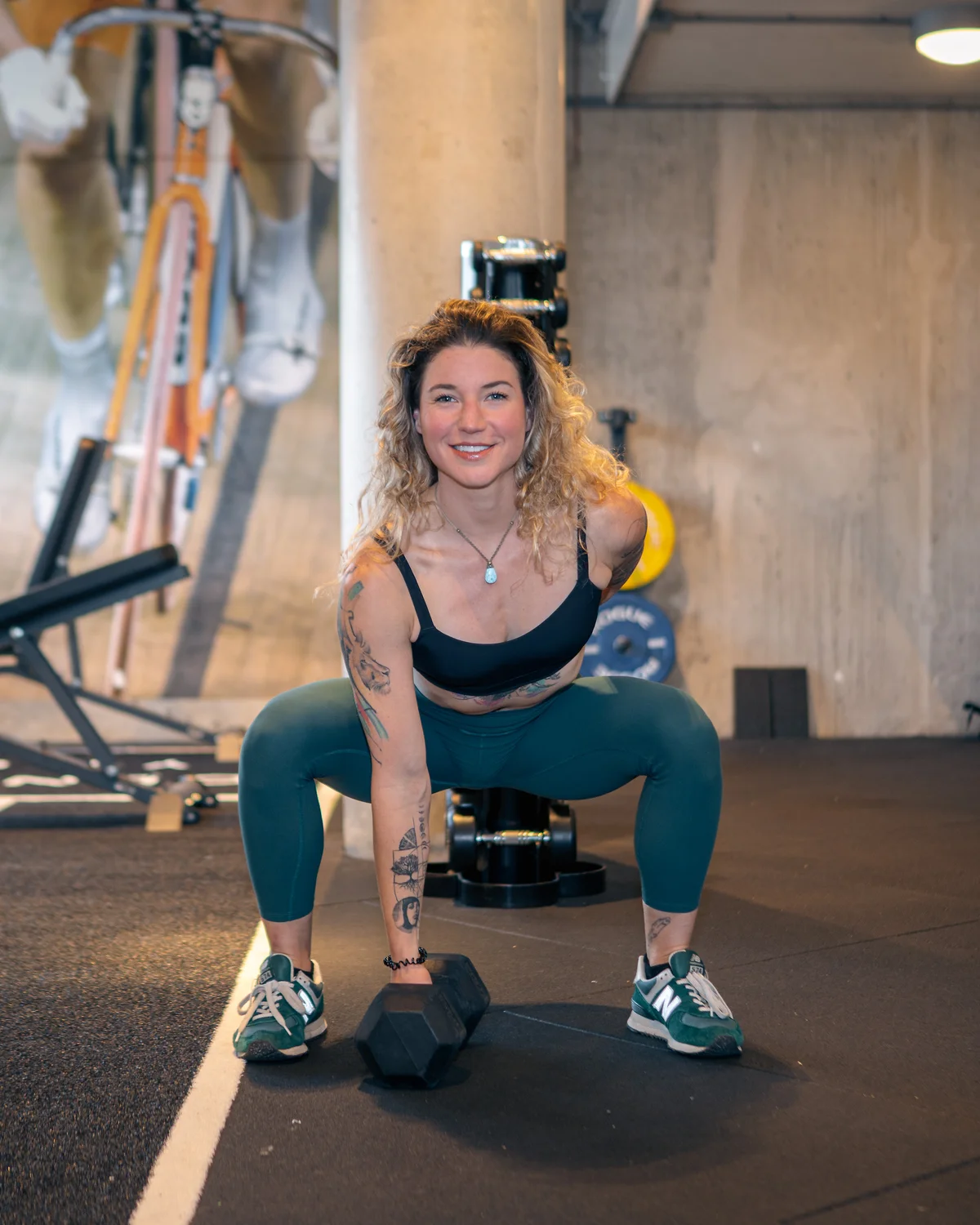 Zoë smiling in a squat, holding a dumbbell, in the gym